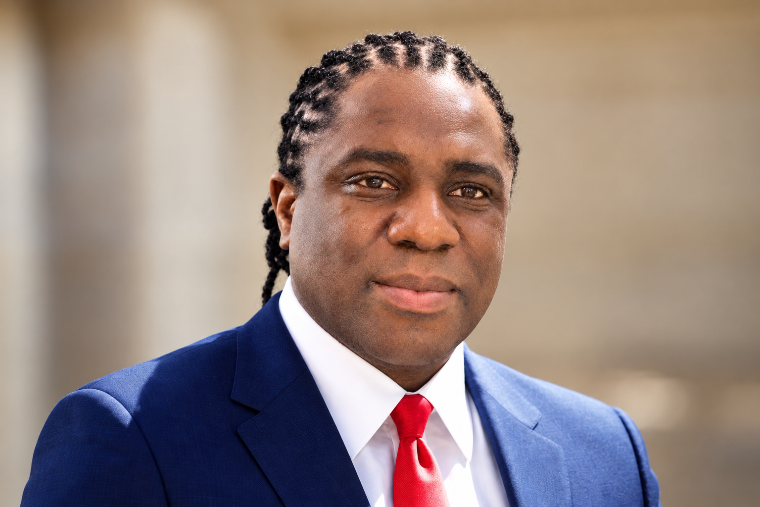 Edited executive portrait of Colin Kasambira wearing a navy suit and red tie